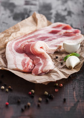 Raw fresh smoked pork bacon slices on butchers paper on dark wooden board with garlic basil.