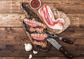 Grilled bacon strips on vintage wooden board with raw fresh smoked pork bacon on butchers paper...