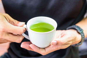 The man hold the hot green tea on his hand before drink / hot matcha