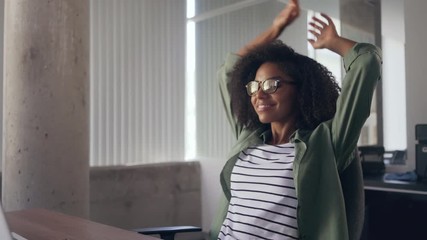 Young woman sitting at desk in front of laptop stretching her arms - Powered by Adobe