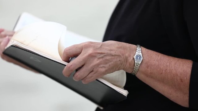 Close up view of two white female hands holding thick black book. Wedding organizer reading a book at a wedding in front of the newlyweds on the beach