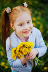 a little girl with red hair smiles against a field of dandelions and green grass. Summer, childhood, holidays