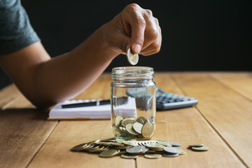 Men are Saint documents about save money and put coin in glass jar on desk on black background.