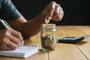 Fototapeta na wymiar Men are Saint documents about save money and put coin in glass jar on desk on black background.