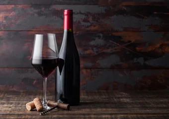 Schilderijen op glas Elegant glas en fles rode wijn met kurken en kurkentrekker op donkere houten achtergrond. Natuurlijk licht © DenisMArt