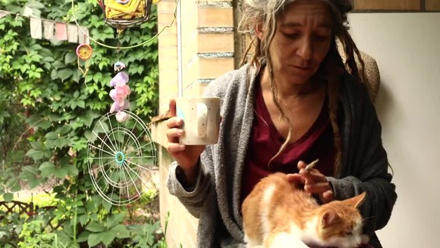 Beautiful adult caucasian woman with long dreadlocks petting little cat cup resting alone outside on summer green backyard dreads braids style freelance lifestyle freedom love peace female person