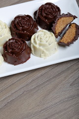 Chocolate coated sweets with almond filling. In the form of a flower. Lie on a white plate. One candy is cut to show the filling.