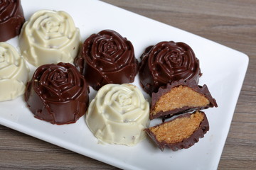 Chocolate coated sweets with almond filling. In the form of a flower. Lie on a white plate. One candy is cut to show the filling.