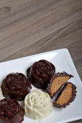 Chocolate coated sweets with almond filling. In the form of a flower. Lie on a white plate. One candy is cut to show the filling.