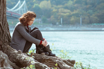 young beautiful brunette depressed sad woman by the river in the city on bridge background