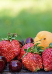 Strawberry, apricot and sweet cherry close-up on the background of summer greens