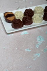 Chocolate coated sweets with almond filling. In the form of a flower. Lie on a white plate. One candy is cut to show the filling.  On an aged surface with peeling paint.