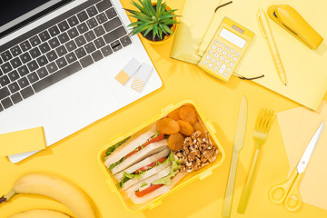 top view of lunch box with food near laptop and office supplies