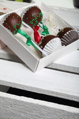 Cake pops decorated with a bow of braid, packed in a gift box. On a wooden box painted white.