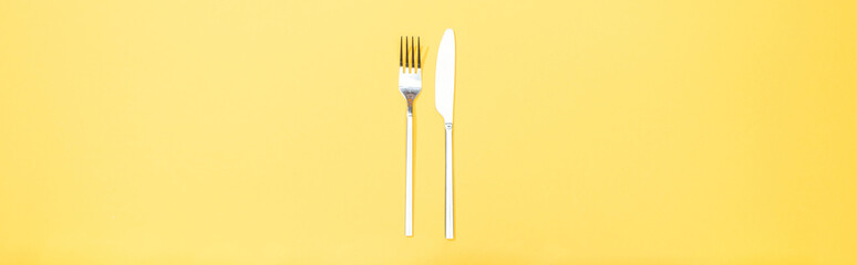 panoramic shot of fork and knife on yellow
