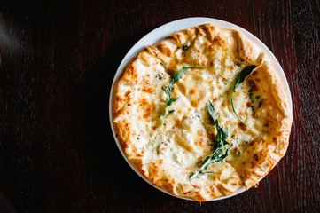 Italian pizza four cheese with arugula on a brown wooden desk background. Quattro FORMAGGI. from top. Delicious hot pizza on a white plate. Galeta.