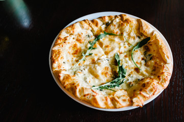 Italian pizza four cheese with arugula on a brown wooden desk background. Quattro FORMAGGI. from top. Delicious hot pizza on a white plate. Galeta.