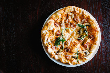 Italian meat pizza with arugula on a brown wooden desk background. Top photo. from top. Delicious hot pizza on a white plate. Galeta.