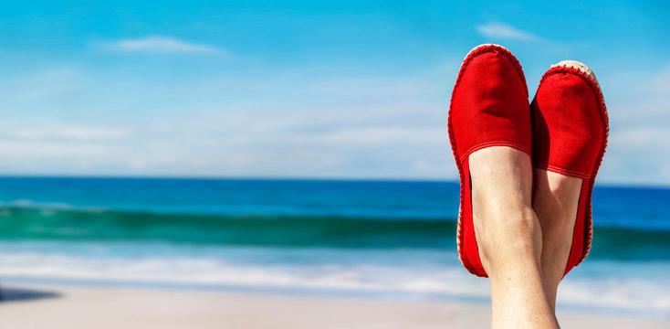Beine mit roten Stoffschuhen vor Strand und Meer