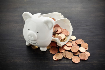 Broken piggy bank with money on dark wooden background