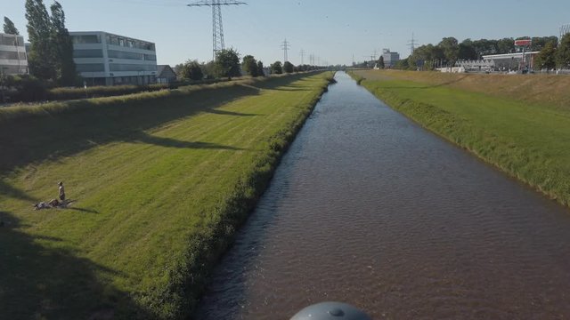 Tracking shot of a small water stream river surrounded by grass and trees under the buke skies from behind the bridge railings in Offenburg, Germany