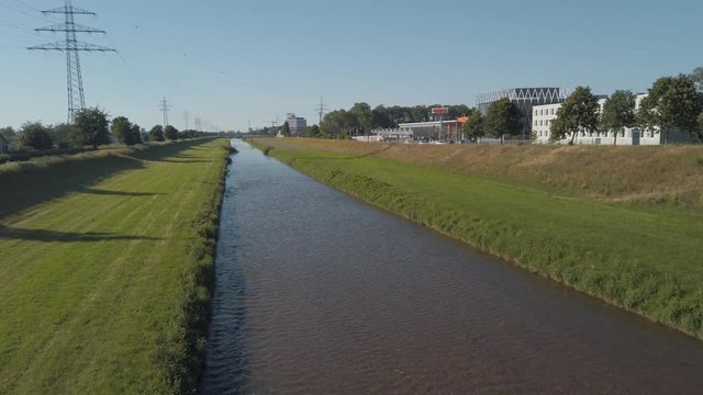 Sliding reveal shot of a small water stream river surrounded by grass and trees under the buke skies from behind the bridge railings in Offenburg, Germany