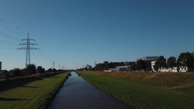 Sliding reveal shot of a small water stream river surrounded by grass and trees under the buke skies from behind the bridge railings in Offenburg, Germany