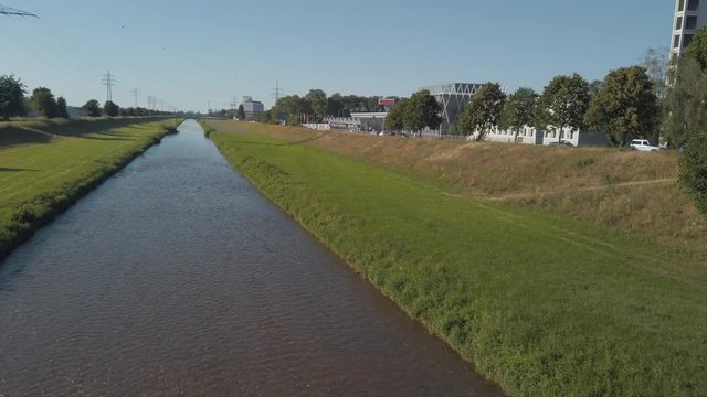 sliding reveal shot of a small water stream river surrounded by grass and trees under the buke skies from behind the bridge railings in Offenburg, Germany