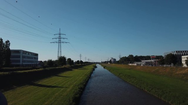 Sliding reveal shot of a small water stream river surrounded by grass and trees under the buke skies from behind the bridge railings in Offenburg, Germany