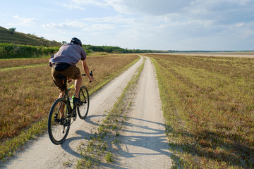 Naklejka premium Cyclist bicycle biker in safety helmet ride high speed landscape from behind