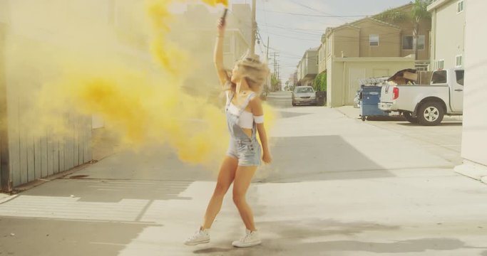 Young hipster girl dancing outside in urban alley with smoke grenade on sunny day 