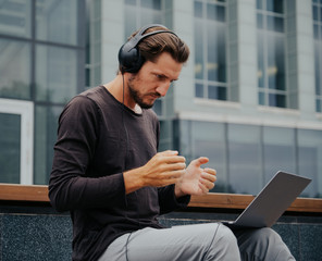 Freelancer Man in the big urban city working with a laptop phone camera and listening music via headphones