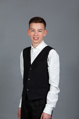 Portrait of happy schoolboy teenager in white shirt and jacket against gray background