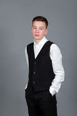 Portrait of happy schoolboy teenager in white shirt and jacket against gray background