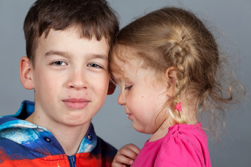 Sister hugs older brother. Studio gray background