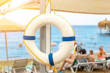 Beautiful white lifebuoy hanged on umbrella at tropical sandy beach. Life saver ring with beautiful blue sea coast on exotic resort. Travel and vacation concept