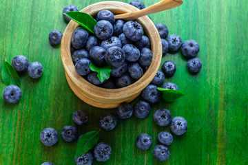 Cranberries in a wooden bowl with a teaspoon with green leaves on a green wooden table