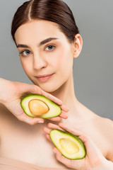 beautiful young woman holding avocado halves isolated on grey
