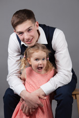 Sister hugs older brother. Studio gray background