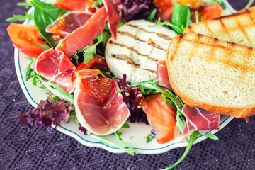Tasty mixed salad dish with grilled camembert cheese, prosciutto ham, organic tomato and fresh green leaves. Healthy dilicious meal. Isolated on black