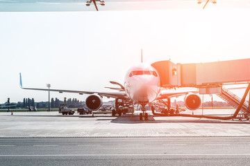 Big modern commercial plane on airfield docked with boarding bridge at sunrise or sunset. Blue clear sky on background. Travel and tourist destination concept