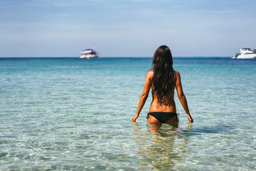 Attractive tanned woman entering into a paradise tropical sea water in a thai beach. Ko Samui, Thailand.