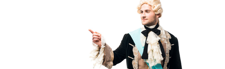 panoramic shot of happy victorian man in wig standing and pointing with finger isolated on white