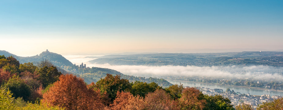  Panoramic view of the hill Drachenfels with the castle ruin, the castle Drachenburg in Siebengebirge and the town Königswinter, morning fog arose from the river Rhine valley, NRW, Germany