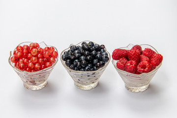 Blueberries, raspberries, currants in glass plates on a white background. Isolated