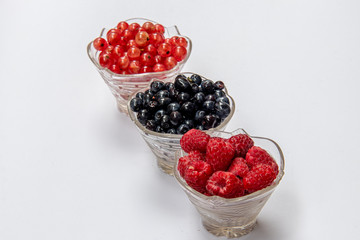 Blueberries, raspberries, currants in glass plates on a white background. Isolated