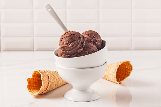 Chocolate ice cream bowl and cones on the white surface.