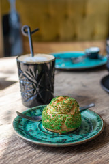 Pistachio eclair, profiterole in glaze on green plate on table, close up. Eclair, custard tart with pistachio cream. Traditional French dessert