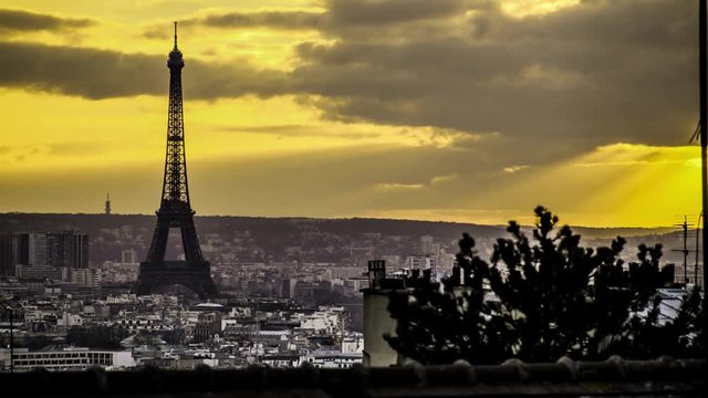 Time lapse of a view of the Eiffel tower and the city of Paris in black and white with a yellow sky and the sun shining through clouds, creating beautiful rays of light