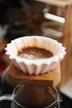 Blooming coffee in pink ceramic origami dripper. On wooden coffee stand. Close up. Alternative manual brewing